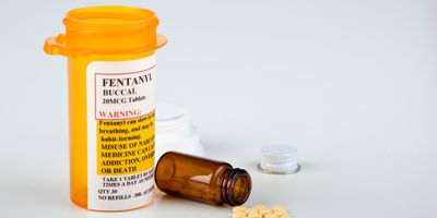 Fentanyl addictive prescription drug bottle with warning labels beside a few pills from an open, fallen vial.