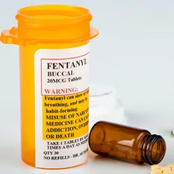 Fentanyl addictive prescription drug bottle with warning labels beside a few pills from an open, fallen vial.
