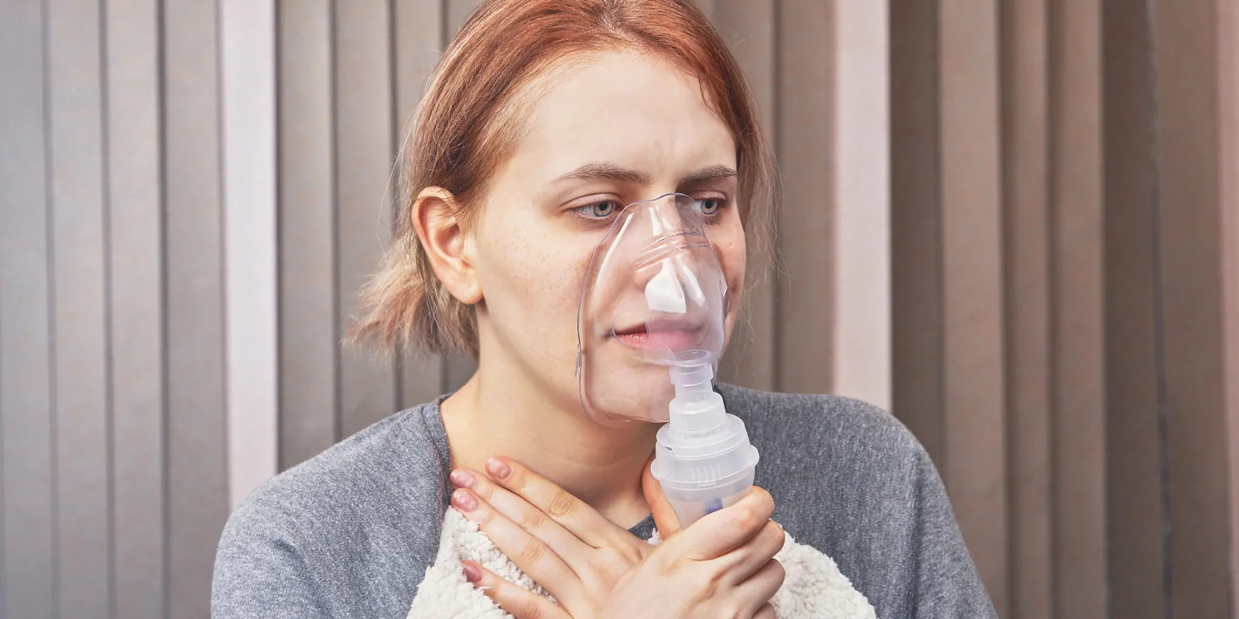 A young woman has an asthma attack and uses a nebulizer chamber for interstitial lung disease to stop it.