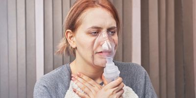 A young woman has an asthma attack and uses a nebulizer chamber for interstitial lung disease to stop it.