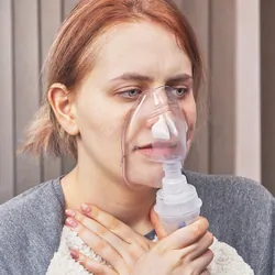 A young woman has an asthma attack and uses a nebulizer chamber for interstitial lung disease to stop it.