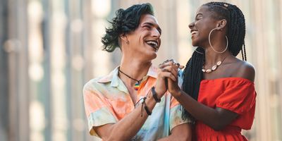Smiling friends, a trans persona and a Black woman, smiling and holding hands.