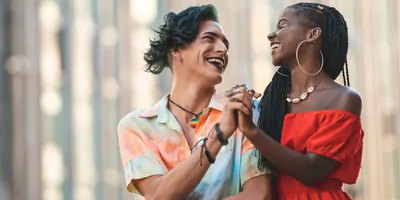 Smiling friends, a trans persona and a Black woman, smiling and holding hands.