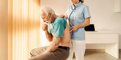 A sick old man coughing and getting medical attention from a female doctor in a doctor's office.