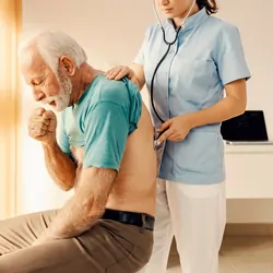 A sick old man coughing and getting medical attention from a female doctor in a doctor's office.