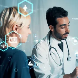 A male clinician discusses a medical report with a woman and points to a screen.