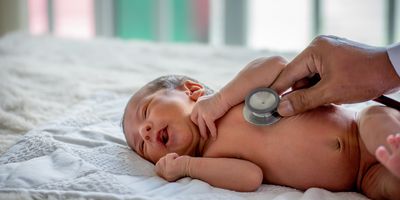 A soft blur of the clinician's hands use a stethoscope to check an infant's health.