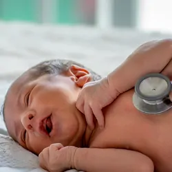 A soft blur of the clinician's hands use a stethoscope to check an infant's health.