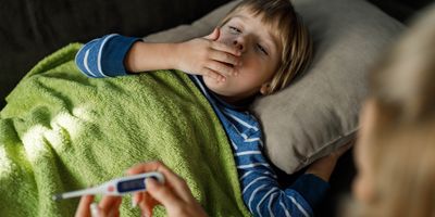 A sick little boy covering his mouth while coughing from fever at home.