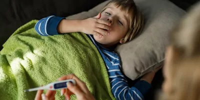 A sick little boy covering his mouth while coughing from fever at home.