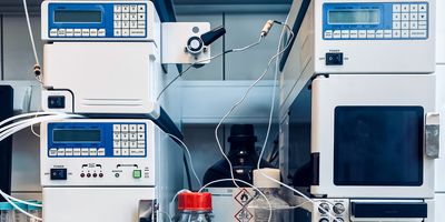 Two machines that comprise an HPLC machine sit across from each other with glass bottles of clear liquid in between them, connected by electrical wires.