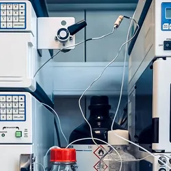 Two machines that comprise an HPLC machine sit across from each other with glass bottles of clear liquid in between them, connected by electrical wires.