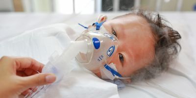 A sick baby boy in a crib wears an inhalation mask with medication to cure Respiratory Syncytial Virus (RSV) at the hospital.