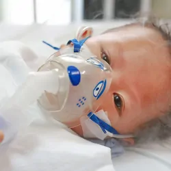 A sick baby boy in a crib wears an inhalation mask with medication to cure Respiratory Syncytial Virus (RSV) at the hospital.