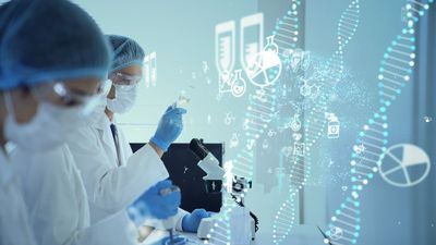 Two researchers wearing hair nets, masks, gloves, and white lab coats examine microscope and liquid filled beakers in a laboratory. Printed DNA strands run across right side of the image. 