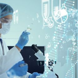 Two researchers wearing hair nets, masks, gloves, and white lab coats examine microscope and liquid filled beakers in a laboratory. Printed DNA strands run across right side of the image. 