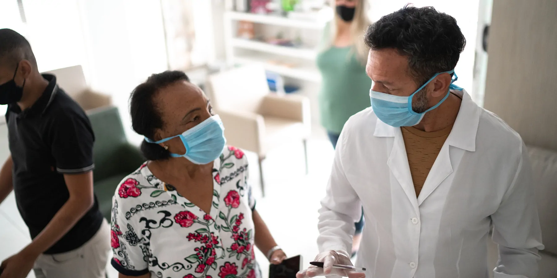 New Series of Trials to Evaluate Long COVID Treatments A female patient talks to a clinician; both wear face masks.