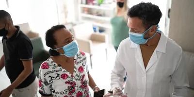 A female patient talks to a clinician; both wear face masks.