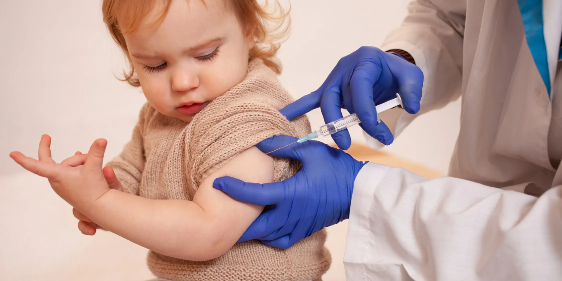 A clinician in PPE vaccinates a child.
