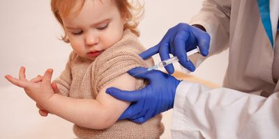 A clinician in PPE vaccinates a child.