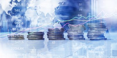 Stack of coins against stock market graphs and a world map to explain finance and inflation.