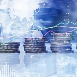 Stack of coins against stock market graphs and a world map to explain finance and inflation.