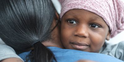 Closeup shot of a child with cancer, wearing a scarf on his head, embracing a female nurse.
