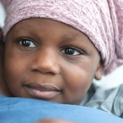 Closeup shot of a child with cancer, wearing a scarf on his head, embracing a female nurse.