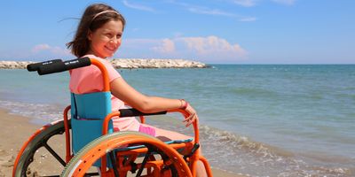 A young little girl in a wheelchair by the sea in the summer