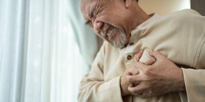 A senior male tugs at his heart in chest pain.