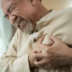 A senior male tugs at his heart in chest pain.