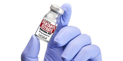 A gloved hand holding a Fentanyl in vial against white background.