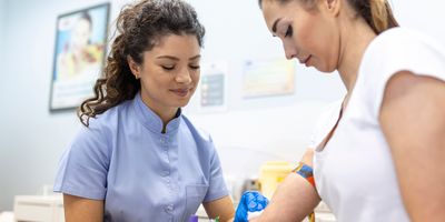 A medical lab technologist with sterile rubber gloves draws blood sample from a female patient.