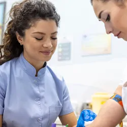 A medical lab technologist with sterile rubber gloves draws blood sample from a female patient.