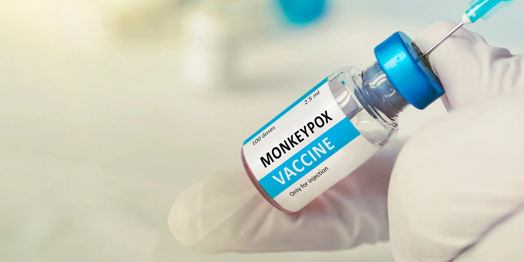 Gloved hands hold a vial of mpox vaccine and load a needle syringe.