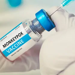 Gloved hands hold a vial of mpox vaccine and load a needle syringe.