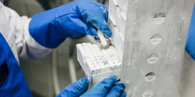 Laboratory worker with blue thermal gloves, a white lab coat and blue apron takes a clear sample tube out of a freezer box