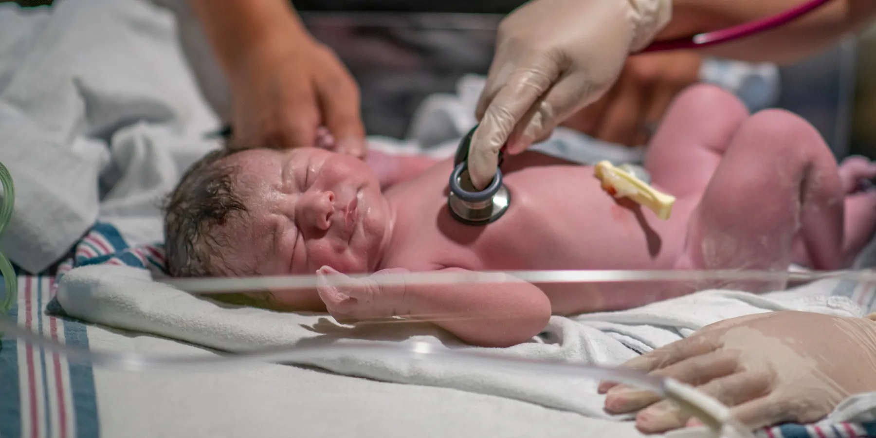 A nurse is holding a stethoscope to the newborn's chest as she listens closely and ensures the baby is in good health.