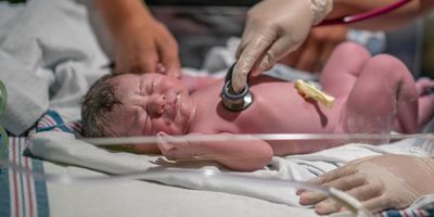 A nurse is holding a stethoscope to the newborn's chest as she listens closely and ensures the baby is in good health.