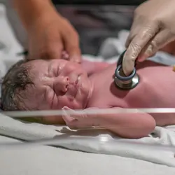 A nurse is holding a stethoscope to the newborn's chest as she listens closely and ensures the baby is in good health.