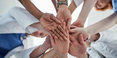 Photo of several clinical lab professionals putting their right hands together in the center of a circle.
