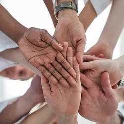 Photo of several clinical lab professionals putting their right hands together in the center of a circle.