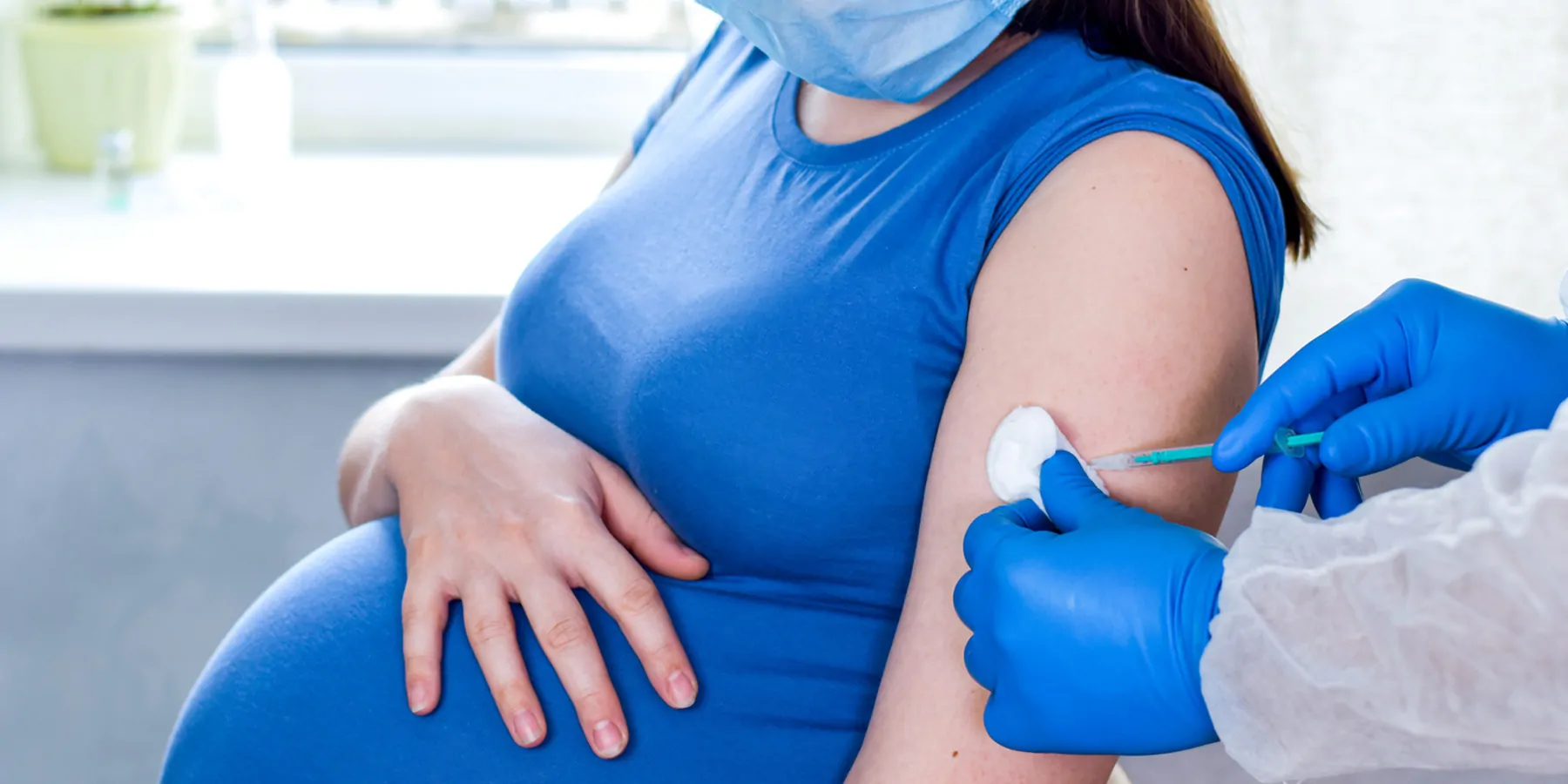 A clinician wearing PPE gives a vaccine injection to a pregnant woman.