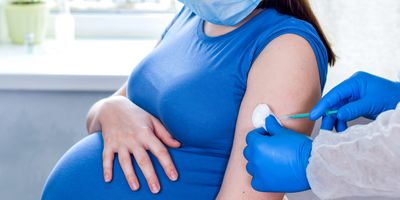A clinician wearing PPE gives a vaccine injection to a pregnant woman.
