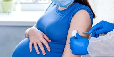 A clinician wearing PPE gives a vaccine injection to a pregnant woman.