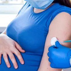 A clinician wearing PPE gives a vaccine injection to a pregnant woman.
