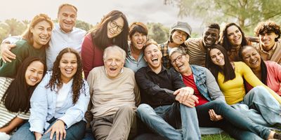 Happy multigenerational people having fun sitting on grass in a public park