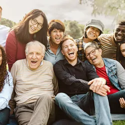 Happy multigenerational people having fun sitting on grass in a public park