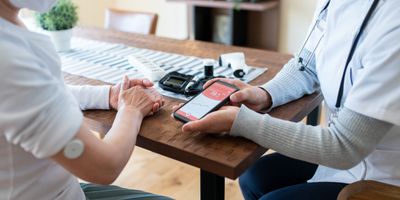 A clinician talks to an elderly patient and uses a smartphone app to check patient's blood sugar levels at home.