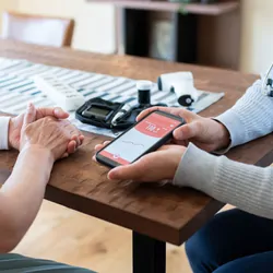 A clinician talks to an elderly patient and uses a smartphone app to check patient's blood sugar levels at home.